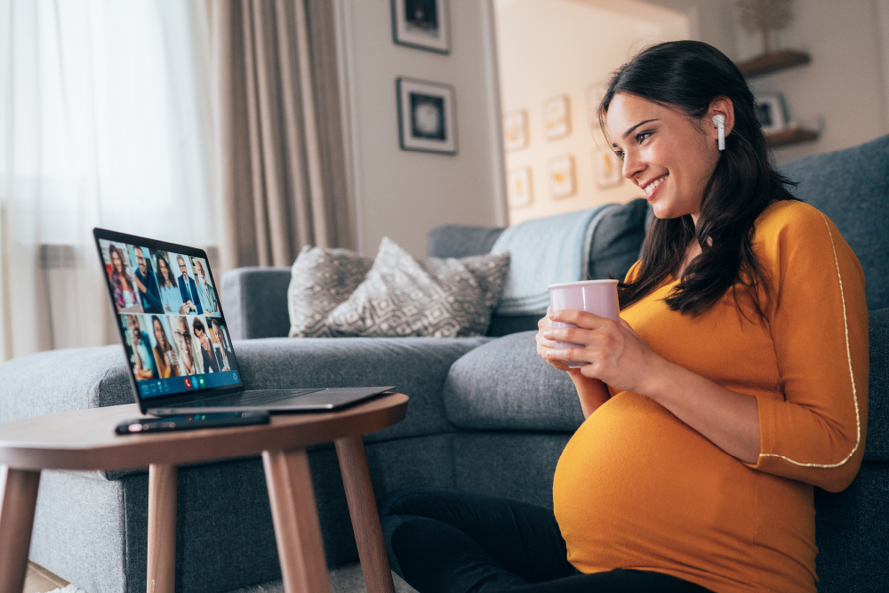 A picture of a pregnant woman sitting on the floor in front of a computer which is on a small table